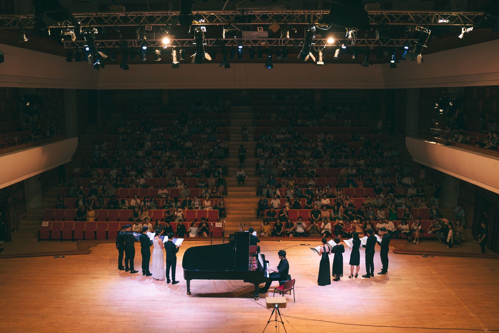 A grand piano and a group of singers performing together on a concert stage
