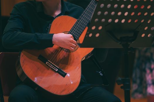 A musician elegantly strums an acoustic guitar in an indoor concert setting.