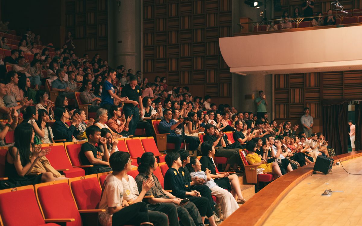 A lively audience applauding in a spacious concert hall, creating energy and excitement.