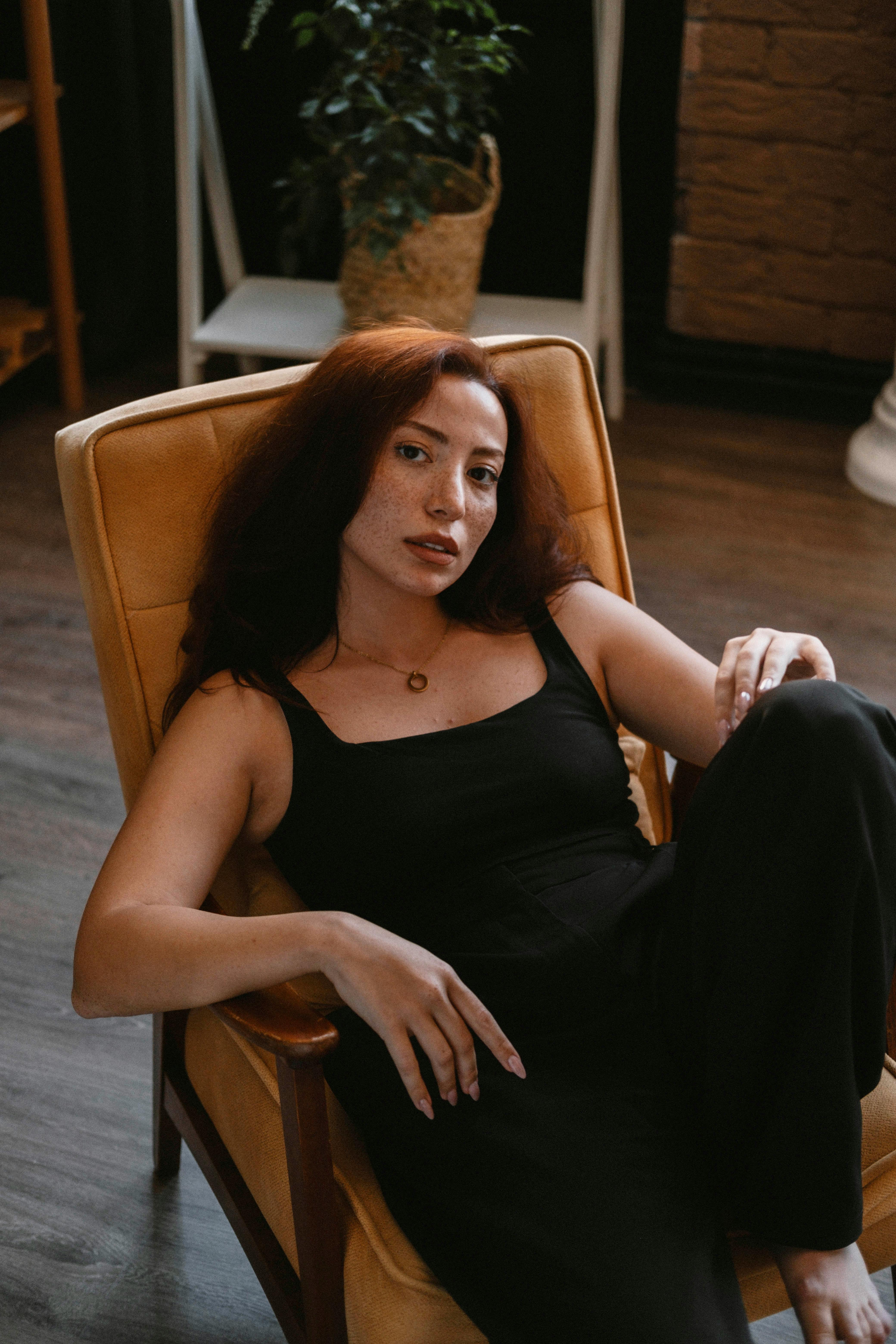 Chic young woman in black attire lounging in a modern armchair indoors.
