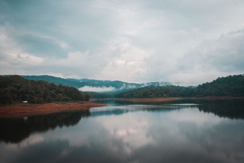 Free Calm lake with misty hills reflecting clouds, perfect for tranquil scenery lovers. Stock Photo