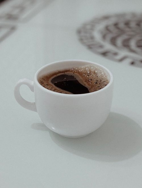 Free A fresh cup of coffee served in a white cup on a glass table with a subtle background design. Stock Photo