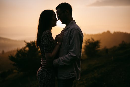 Silhouetted couple embracing romantically at sunrise in a mountainous landscape.