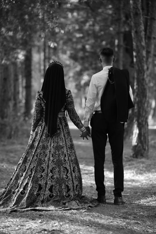 Back View of Couple in Dress and Shirt Holding Hands in Forest