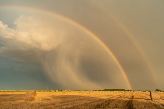 Breathtaking view of a double rainbow arching over a rural field with bales of hay.