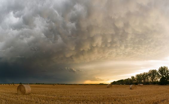 Storm clouds over hay bales in a rural field at sunset.. storm, clouds, over