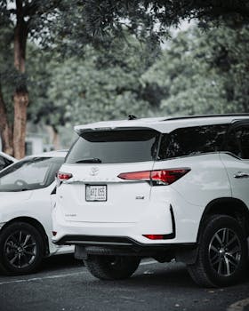A white Toyota Fortuner parked outdoors in a lush green setting, highlighting luxury and style.