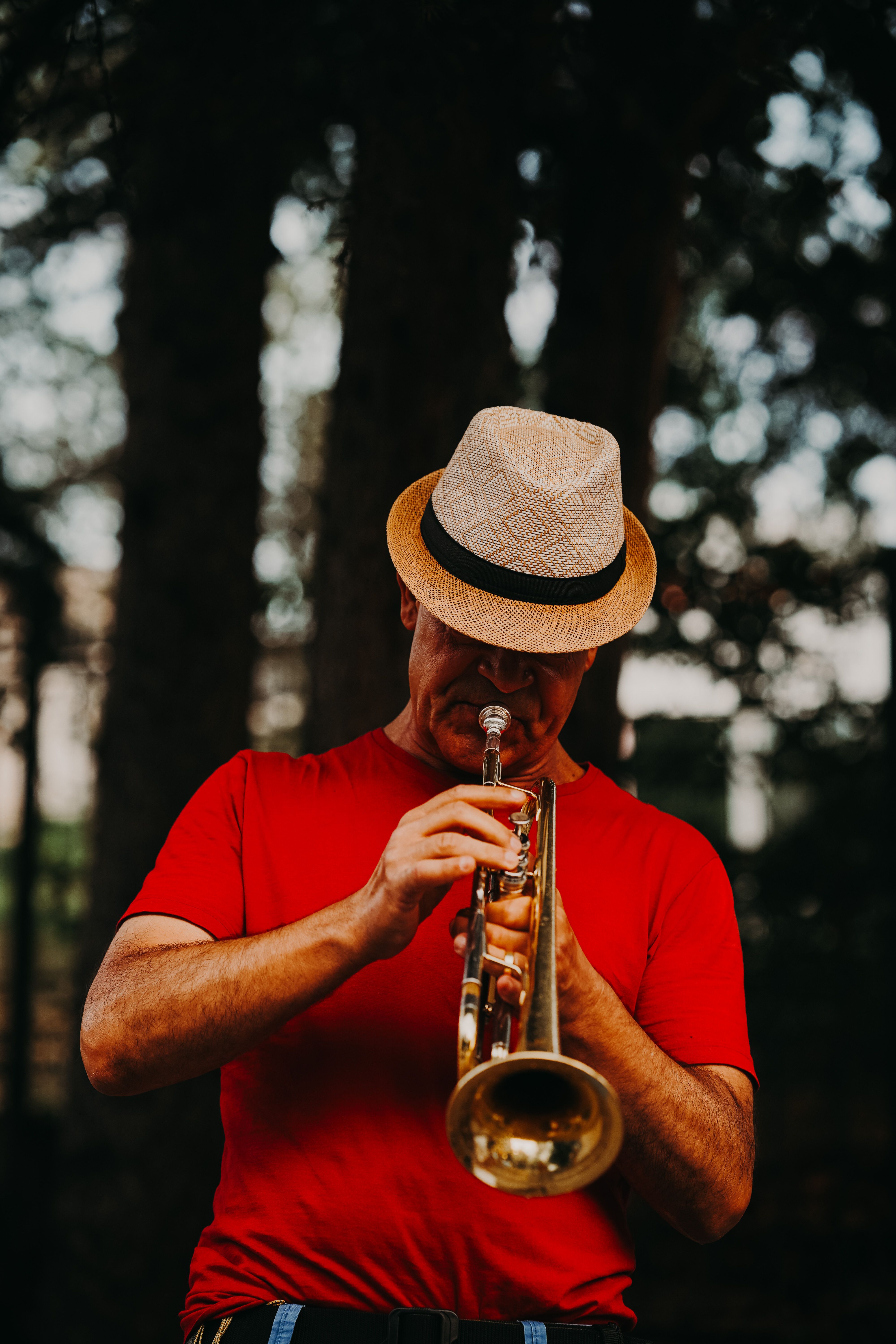 Man in red shirt and hat plays trumpet outdoors in Ankara, Türkiye.