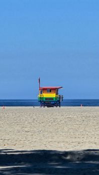 Vibrant rainbow lifeguard tower on a sunny beach with clear blue skies.