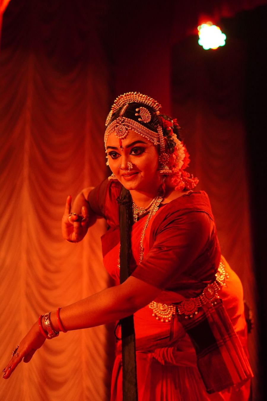 Indian classical dancer in traditional costume under red stage lighting