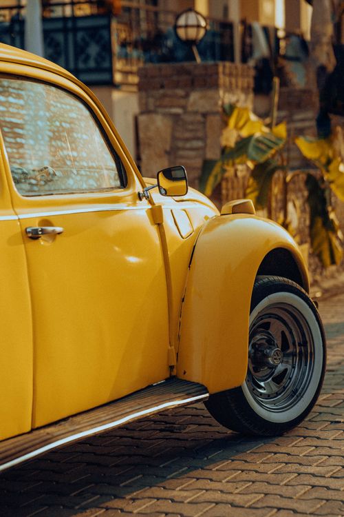 Free Close-up of a vintage yellow Volkswagen Beetle parked on a sunny street, showcasing its classic retro style. Stock Photo