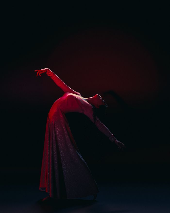 Kathak dancer in a flowing crimson costume on a dark stage