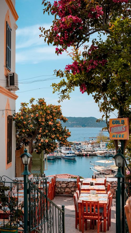 Free Outdoor café by the sea with boats and vibrant flowers, perfect for tourists. Stock Photo