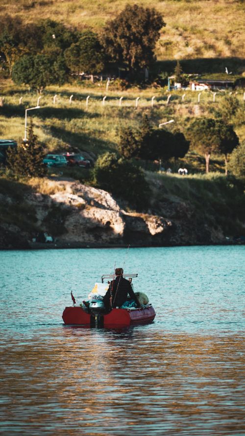 Free A peaceful moment on the lake with a red boat and lush landscape at sunset. Stock Photo