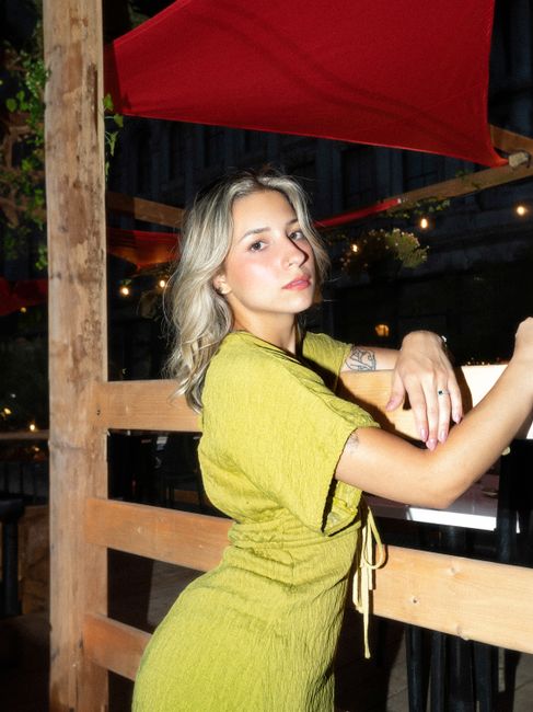 Stylish young woman posing outdoors in a lime green dress under nighttime urban lights.