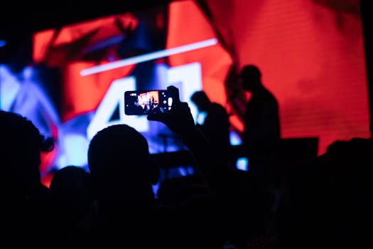 Silhouettes capturing live performance with smartphone, vibrant lights.