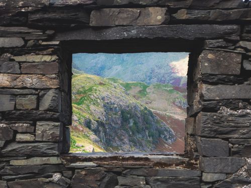 Free A stone wall window frames a stunning summer mountain landscape. Stock Photo