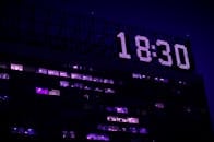 一座现代建筑在夜间亮起灯光，一个醒目的数字时钟显示着18：30