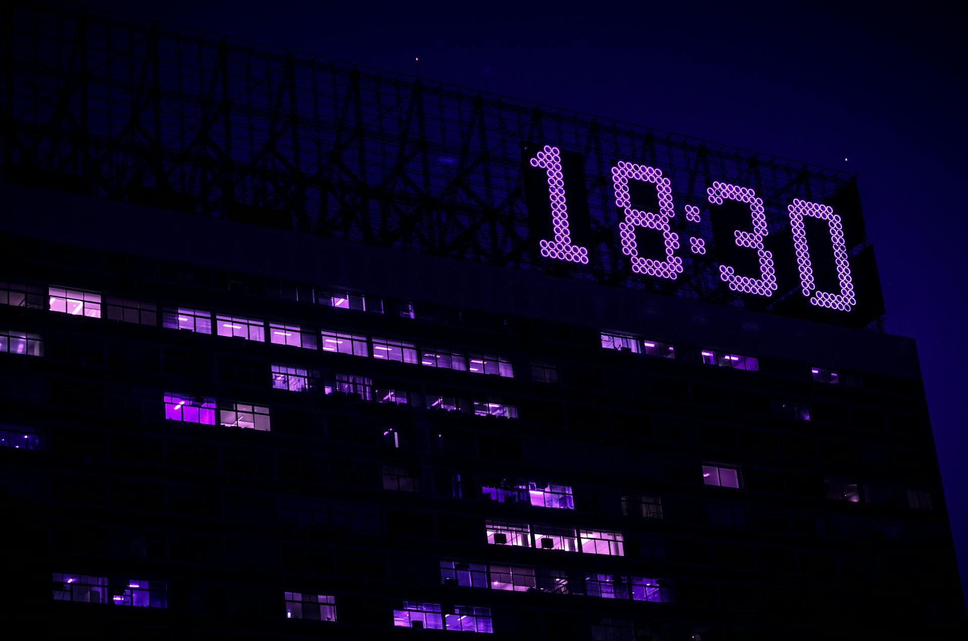 A modern building is illuminated at night with a prominent digital clock showing 18:30.