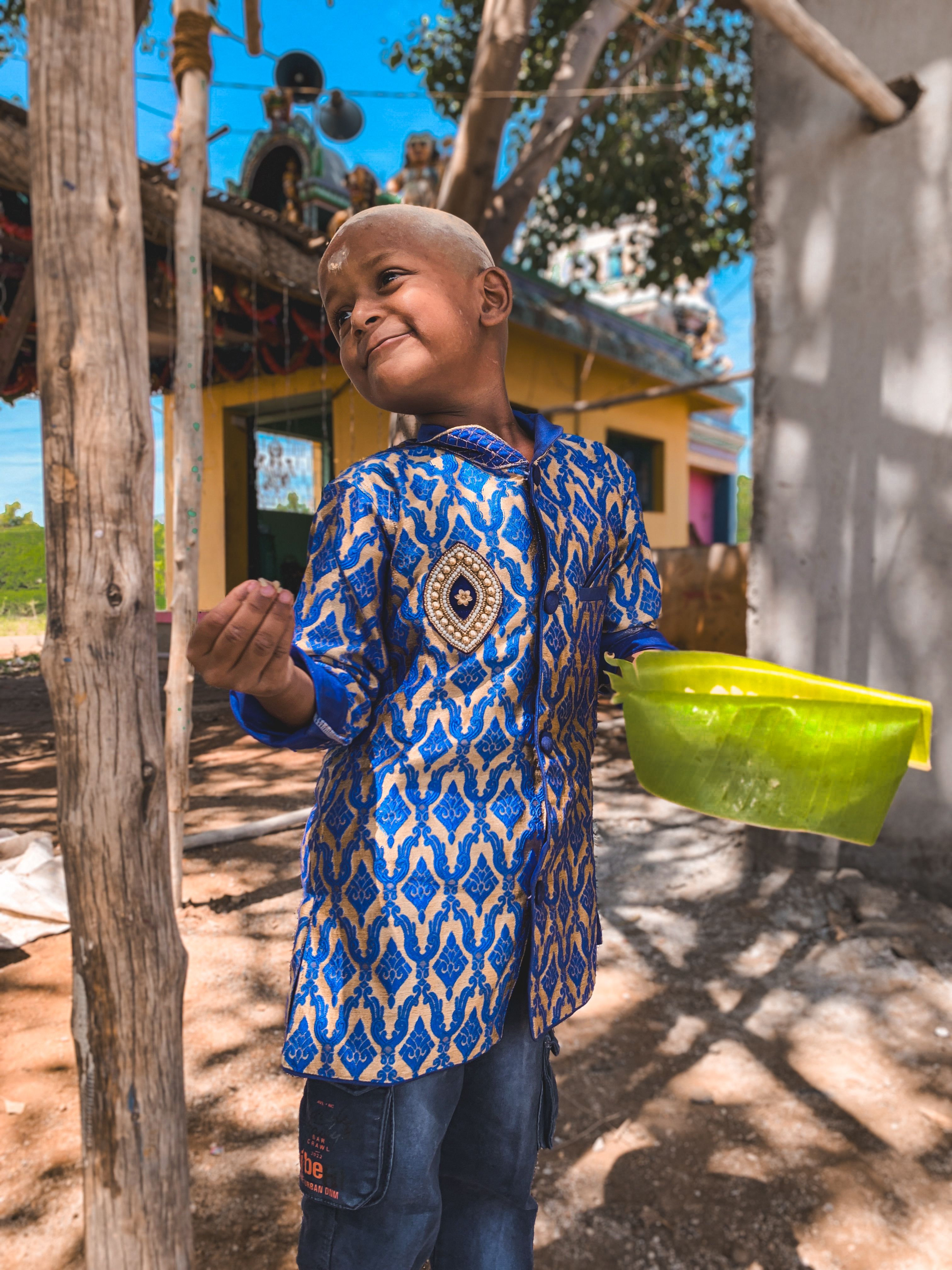 Smiling child in vibrant clothing outdoors on a sunny day with a yellow bucket.