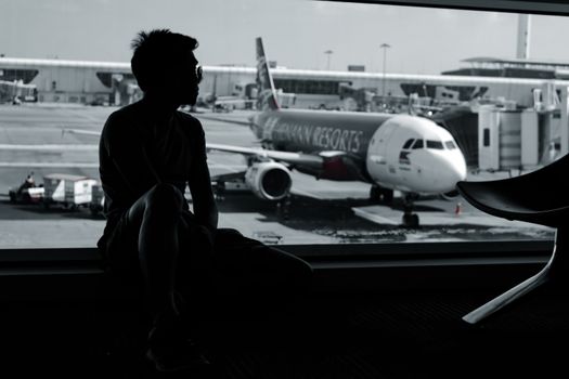 A silhouetted man sits in an airport terminal, viewing an airplane on the tarmac.
