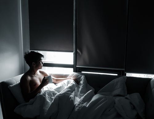 Free Shirtless man enjoying a quiet morning with coffee on a couch near a window. Stock Photo