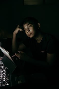 A thoughtful Asian man using a tablet in a dimly lit room, creating a moody atmosphere.
