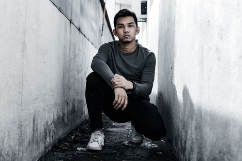 Free A man crouching in a narrow alley, showcasing urban style and mood. Stock Photo
