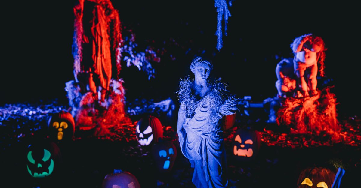 A spooky Halloween display featuring illuminated pumpkins and eerie sculptures at night.