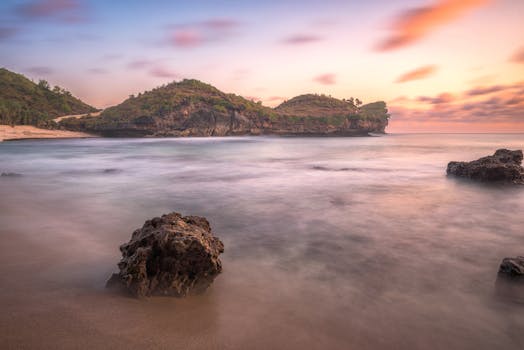 Beautiful sunrise over a tranquil Indonesian beach, with gentle waves and rocky landscape.
