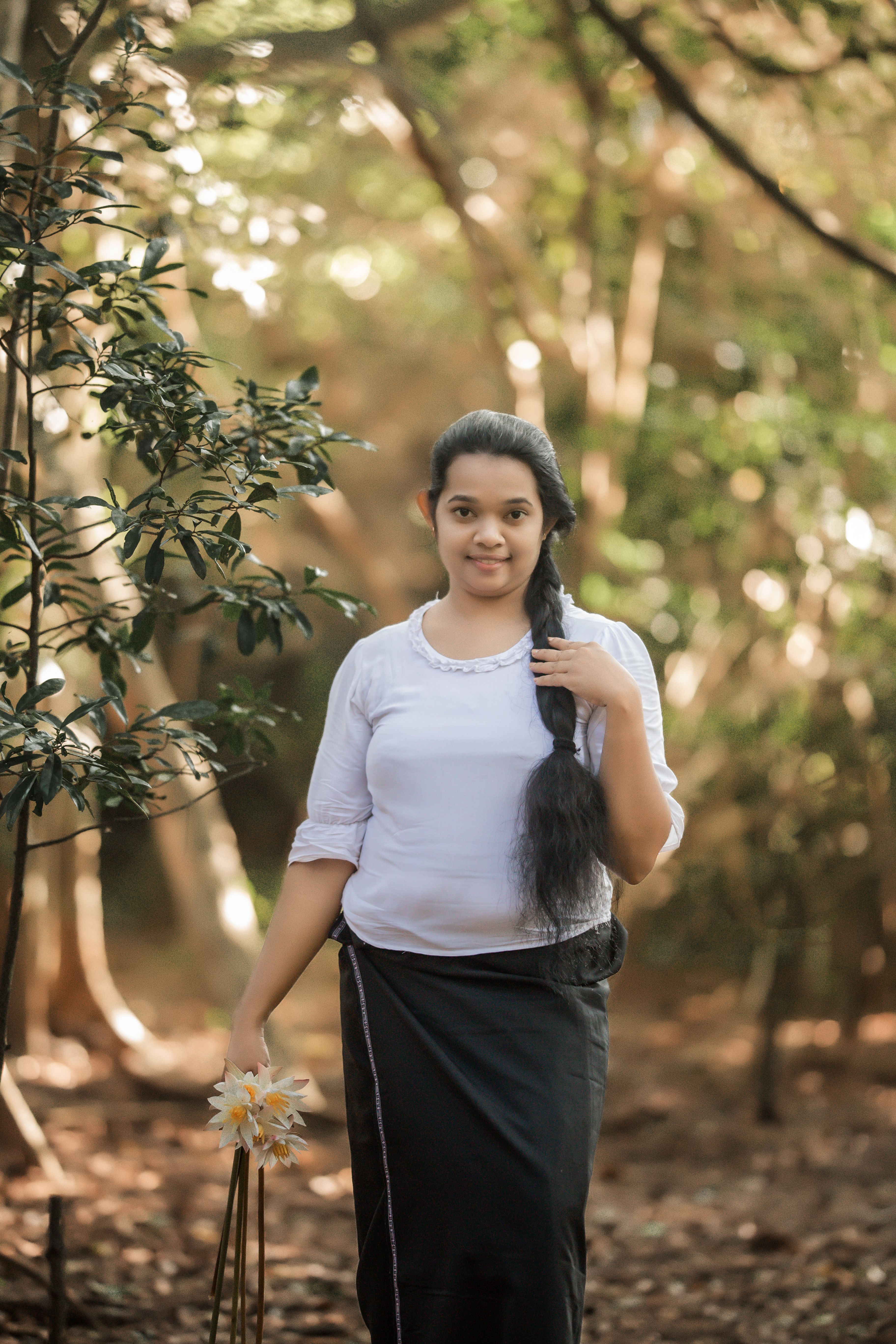 A serene portrait of a woman standing in a forest, showcasing long braided hair and traditional attire.