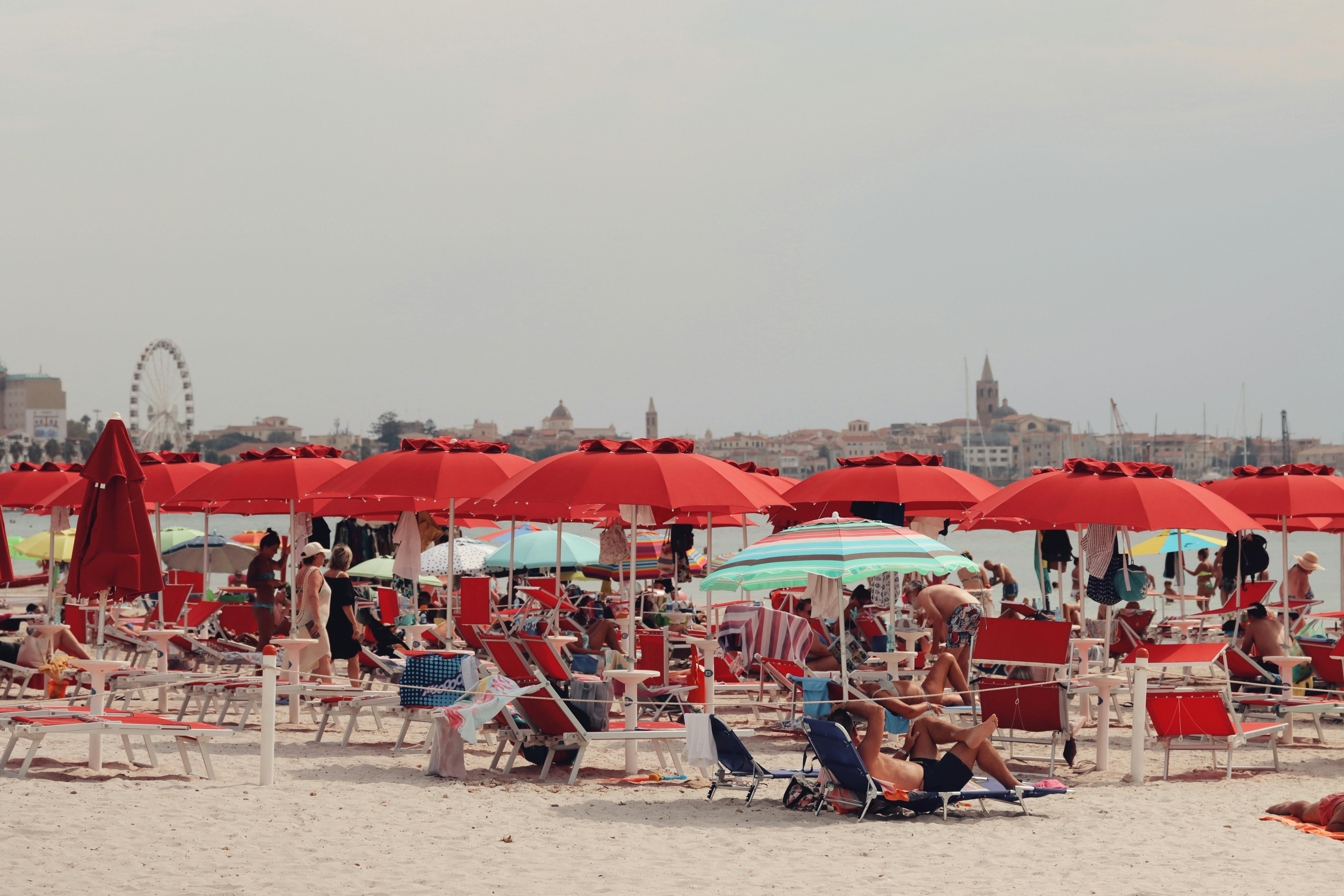 Tourists enjoy the sunny day under red umbrellas at Alghero Beach, Sardinia, Italy.