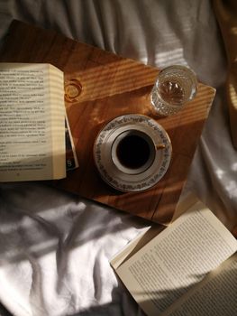 A peaceful morning setting featuring a cup of coffee, books, and a glass on a tray, captured in warm sunlight.