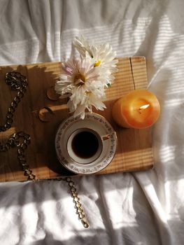 Elegant flat lay of coffee, flowers, and a candle on a wooden tray, perfect for a cozy morning vibe.