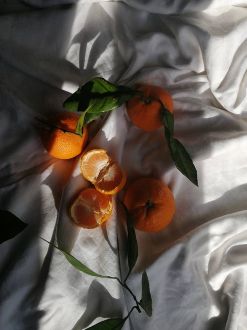 Free Juicy tangerines with leaves on a textured white fabric in dramatic light. Stock Photo