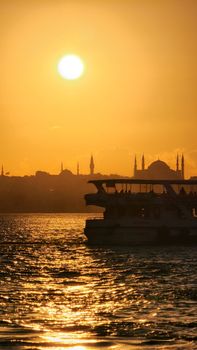 A ferry sails on the Bosphorus against a vibrant Istanbul sunset with iconic mosque silhouettes.