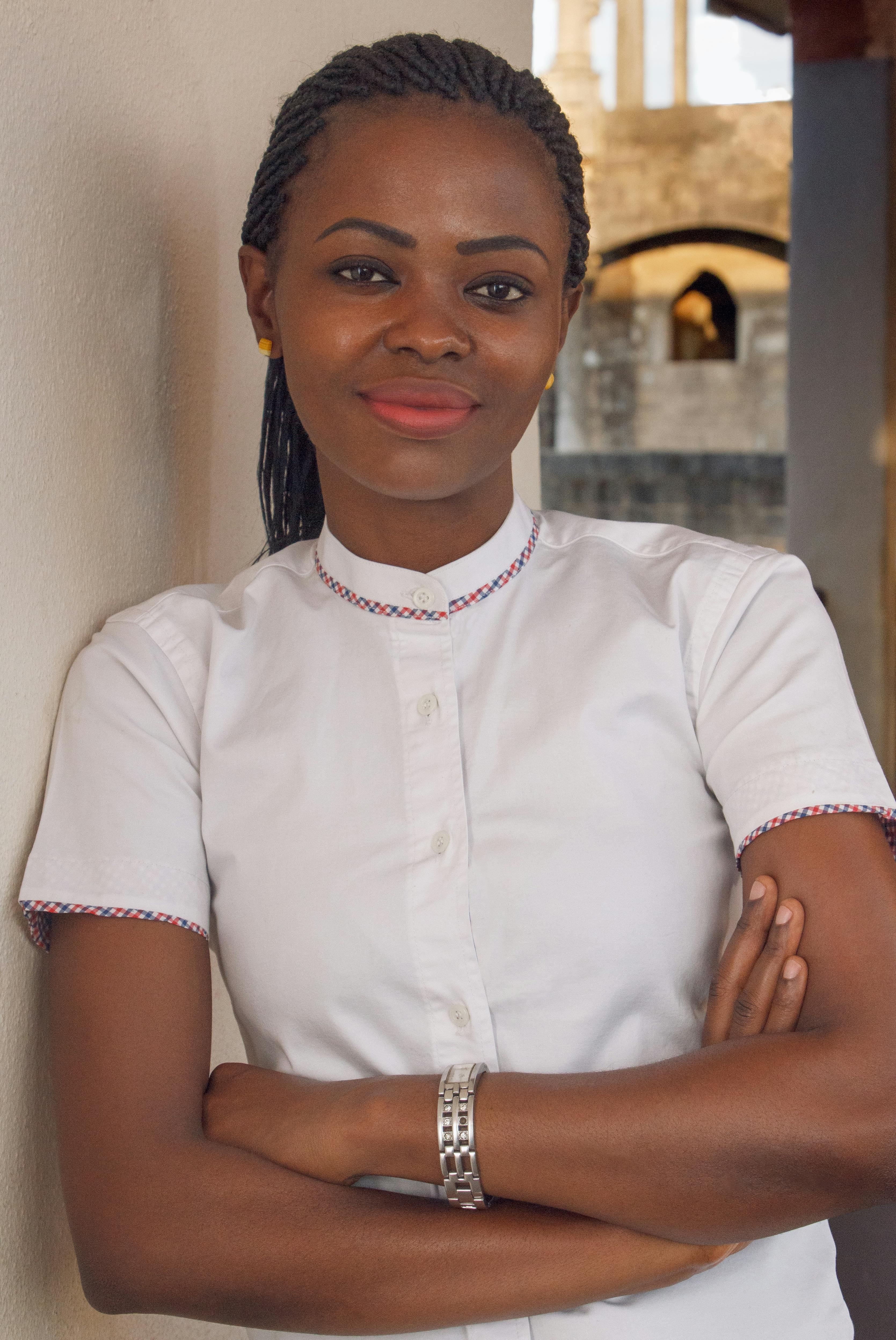 Portrait of a confident young woman in a white shirt with arms crossed, smiling outdoors.