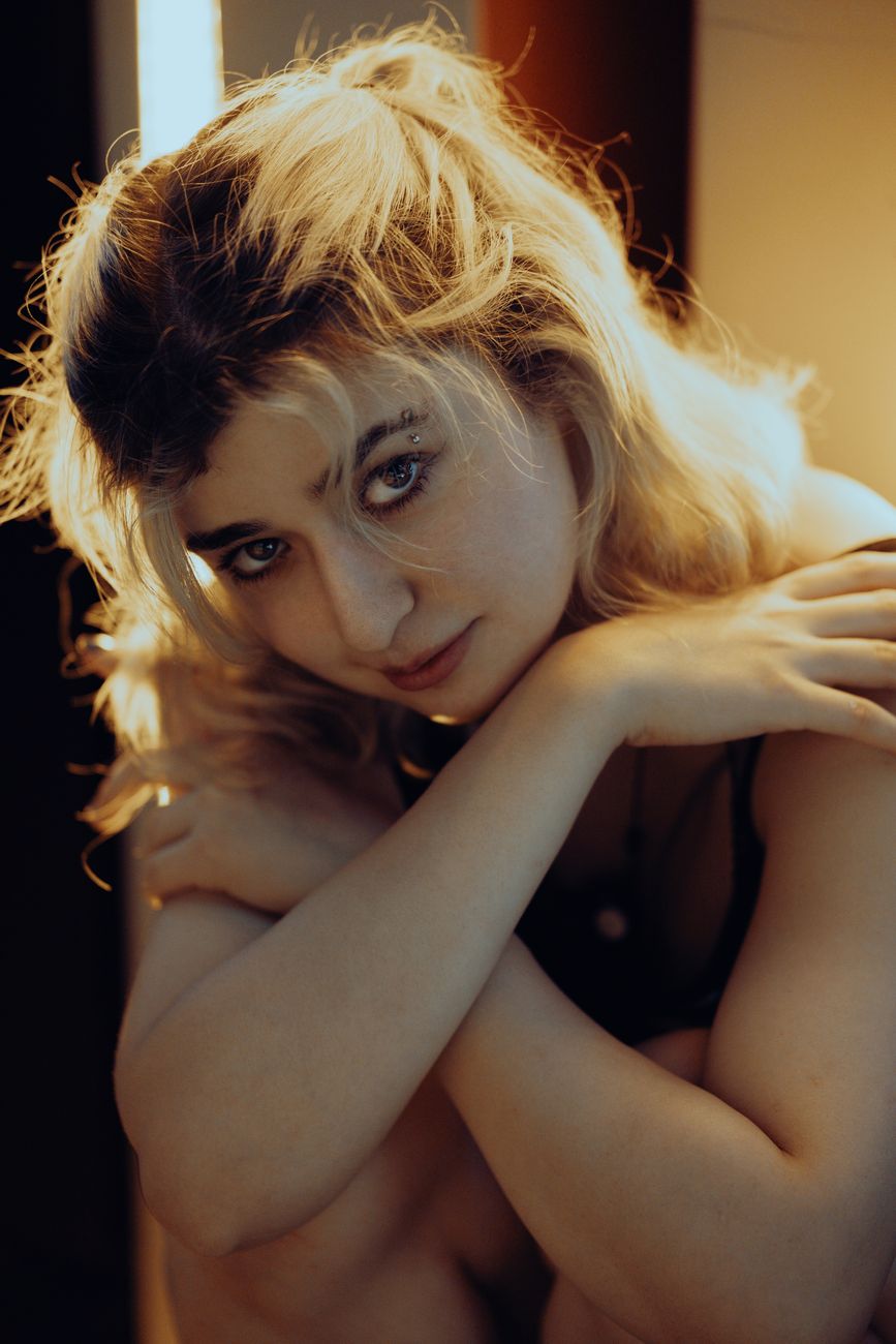 Close-up portrait of a smiling woman with crossed arms, softly lit indoors.