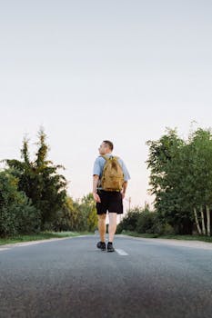 A man with a backpack walking down a forest road in summer, enjoying nature and travel.