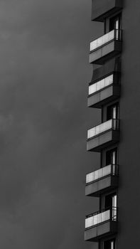 Black and white photo of a modern building's balconies under an overcast, stormy sky.