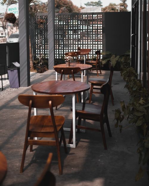 Free A sunlit outdoor cafe patio with wooden tables and chairs, ideal for a relaxed meal. Stock Photo
