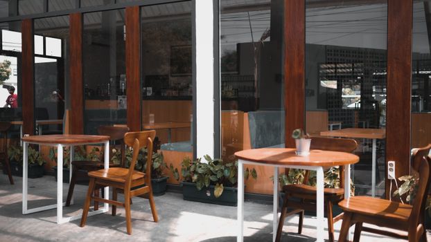Wooden chairs and tables outside a modern cafe with large windows and plant decor.