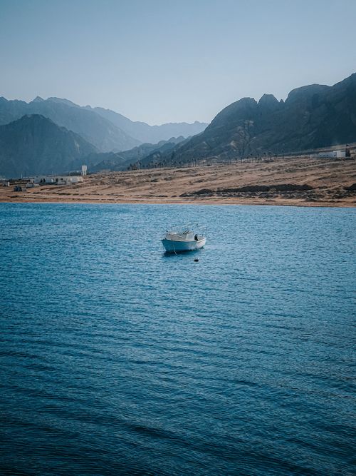 Free Peaceful lake view with a lone boat surrounded by mountains and a clear blue sky. Stock Photo