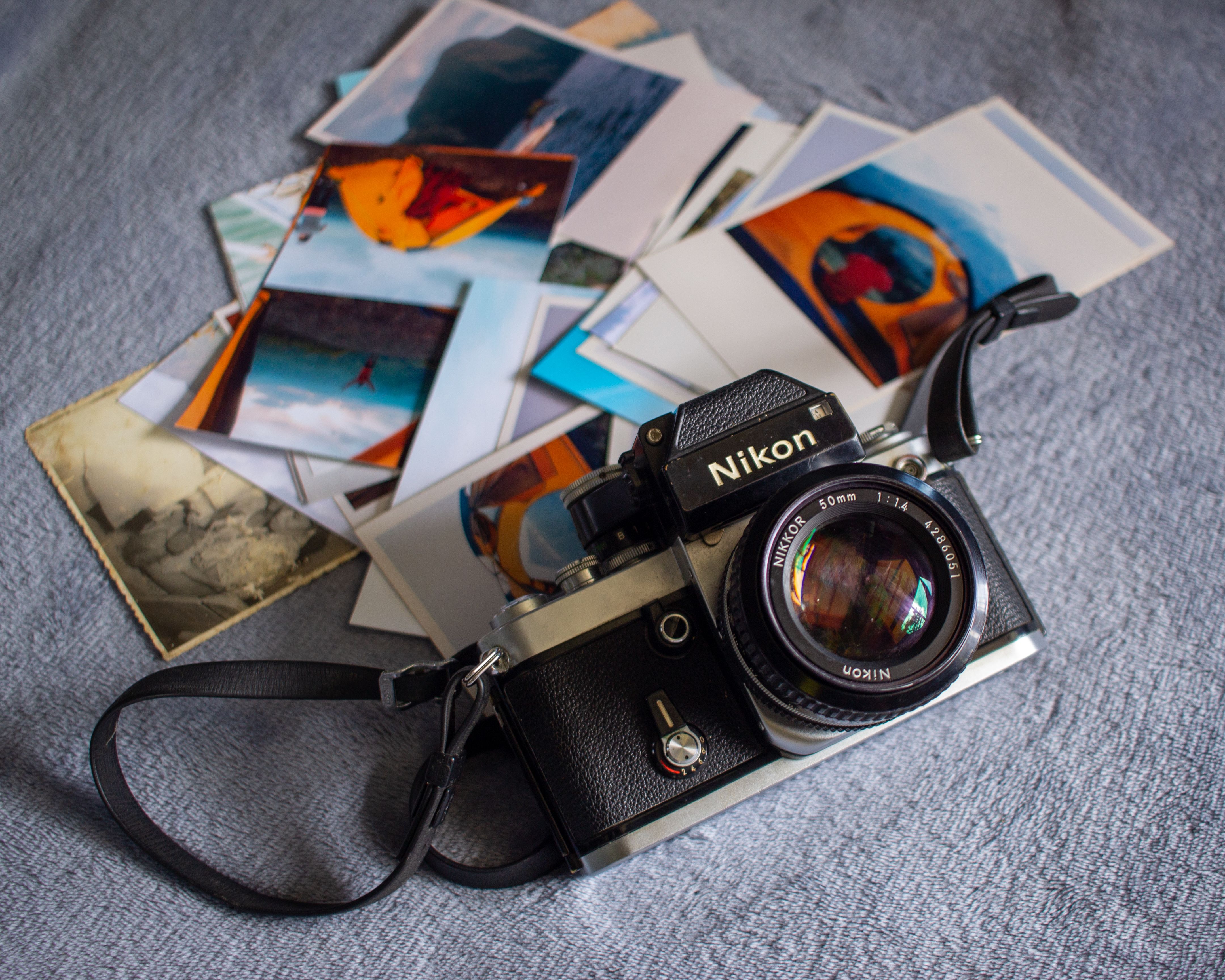 Classic Nikon film camera surrounded by nostalgic printed photographs on a textured surface.