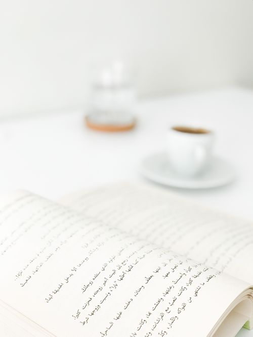 Free A serene setup featuring an open book with Arabic script and a blurred coffee cup in the background. Stock Photo