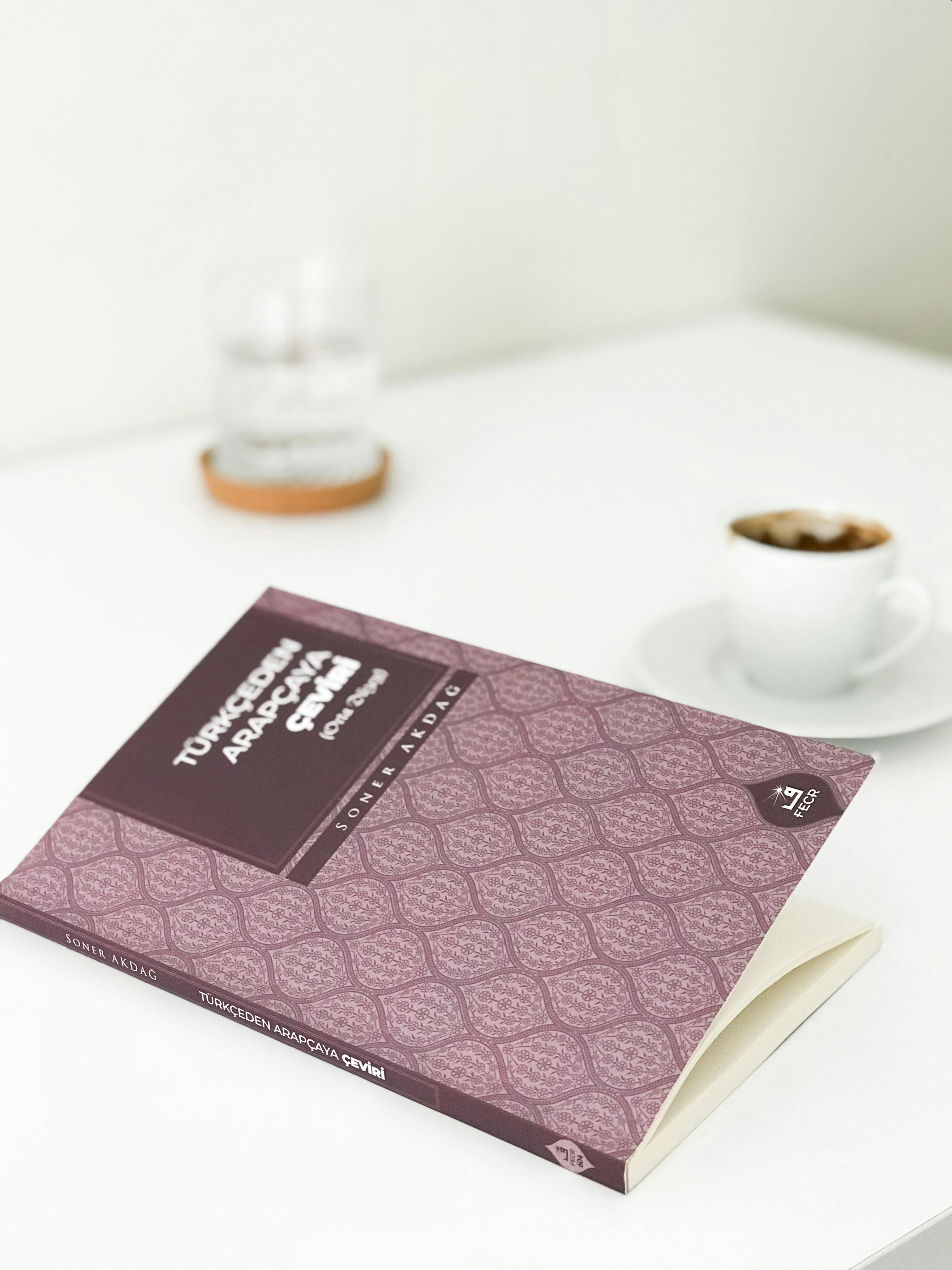 A close-up of a book with a coffee cup in a bright, minimalist setting.