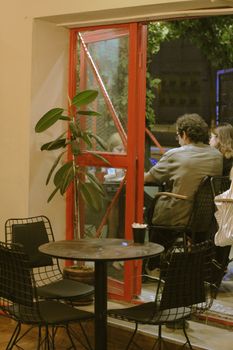 A group of friends enjoying a warm evening at a stylish café with open windows and modern decor.