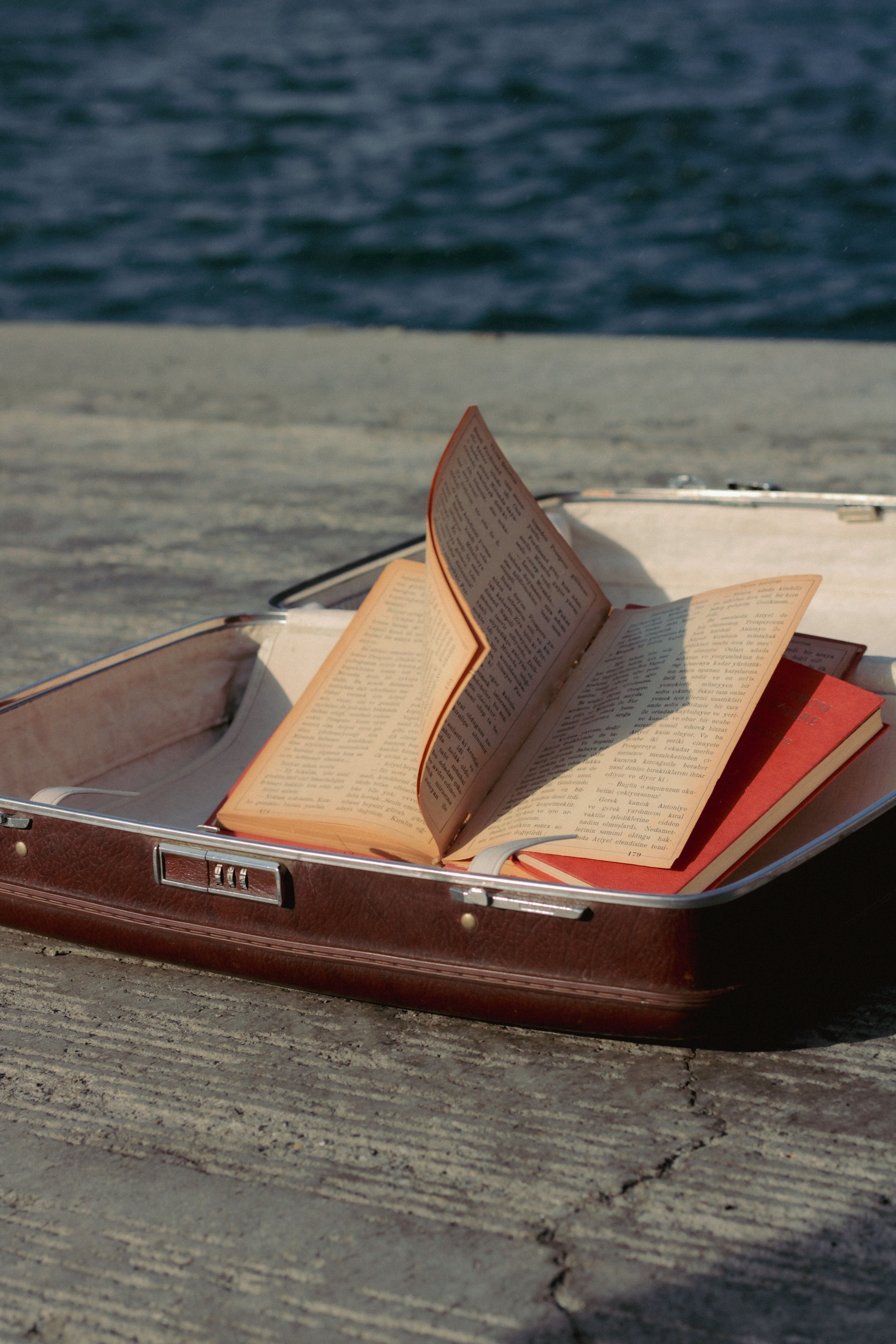 An open vintage book placed in a suitcase by the seaside, evoking nostalgia and travel.