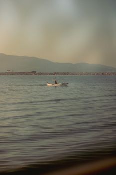 Single boat floats on calm sea during a peaceful evening, surrounded by distant hills.