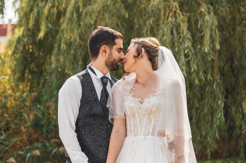 Free A loving couple shares a tender moment in their wedding attire surrounded by lush greenery. Stock Photo